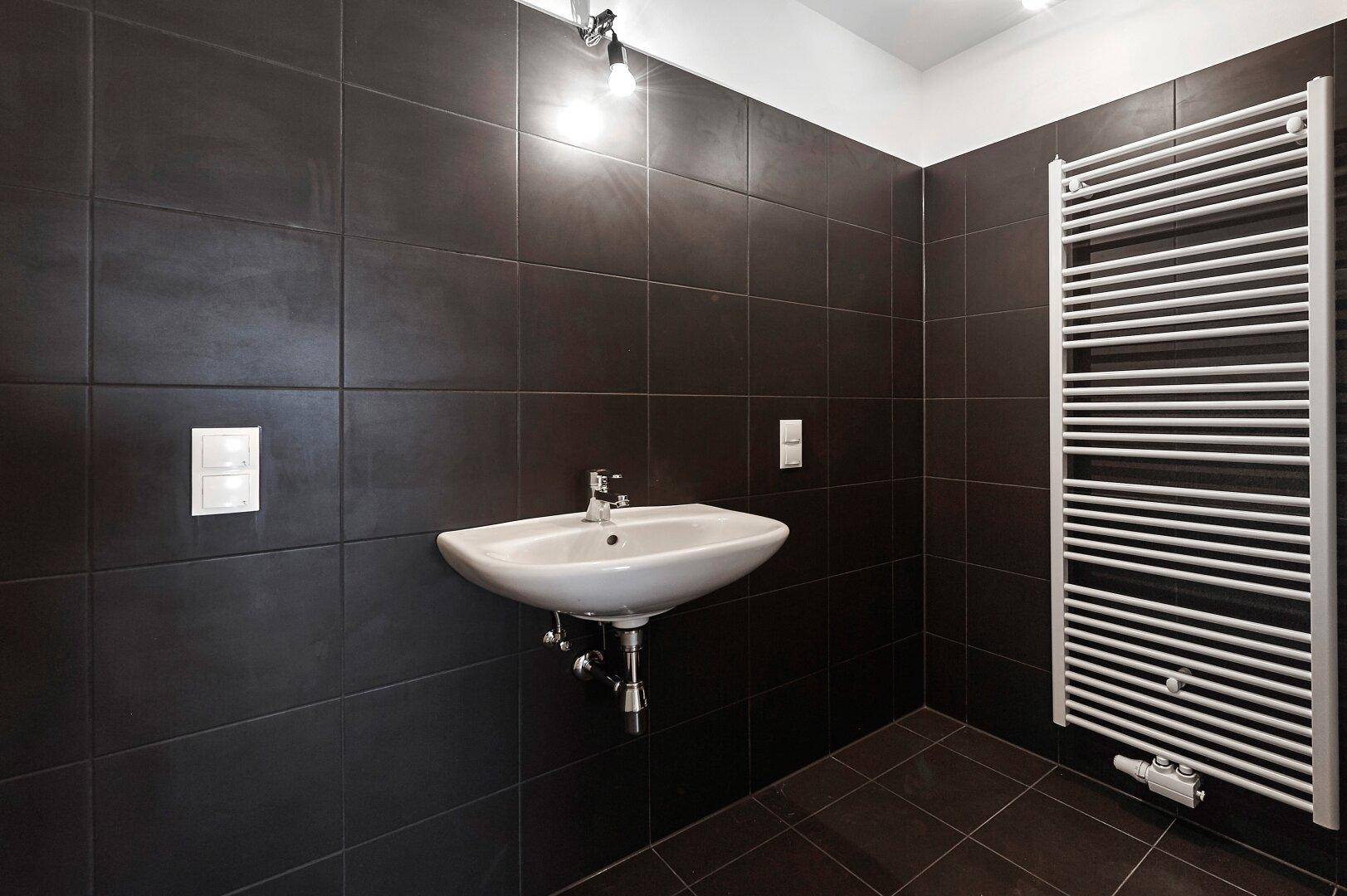 Modernes Badezimmer mit dunklen Fliesen, einem Waschbecken und einem Handtuchheizkörper.