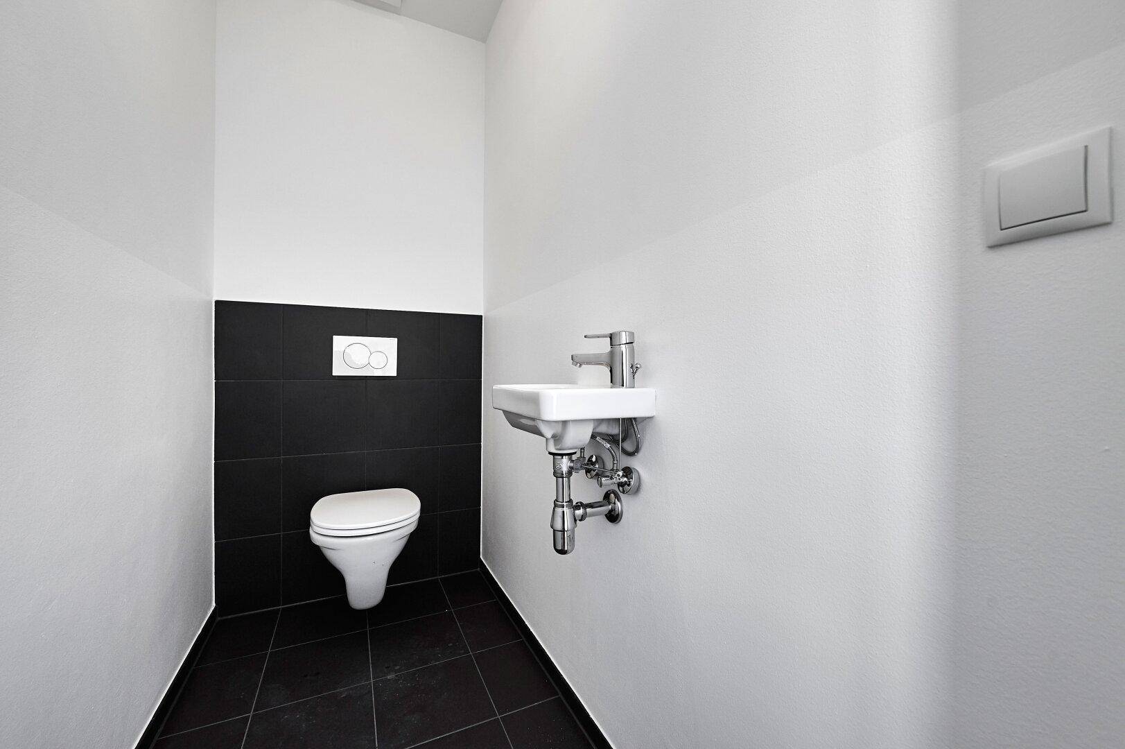 Helles Gäste-WC mit schwarzem Fliesenband, Toilette und kleinem Handwaschbecken.