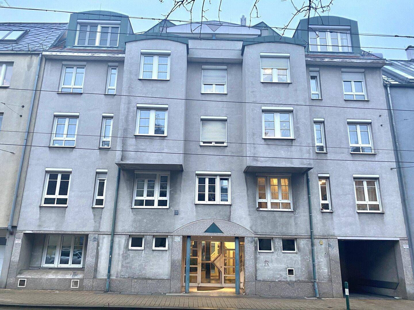 Die Fassade eines Mehrfamilienhauses mit zahlreichen Fenstern, Rollläden und einem modernen Eingangsbereich.