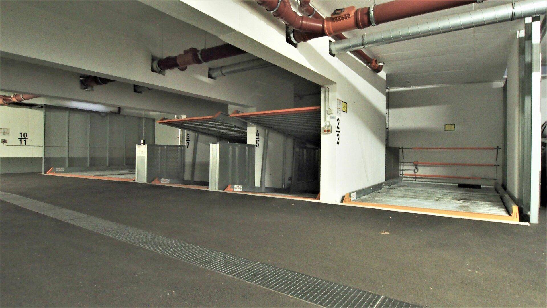 Tiefgarage mit mechanischen Parksystemen und sichtbaren Rohrleitungen an der Decke.