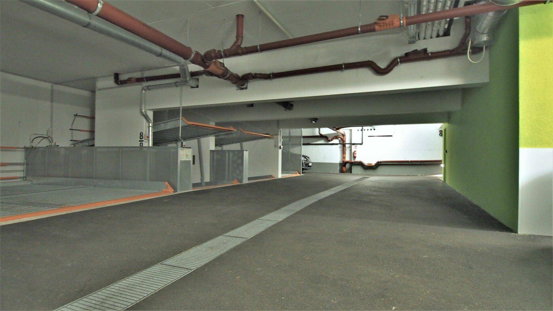 Geräumige Tiefgarage mit Fahrspur, Parksystemen und grüner Akzentwand.