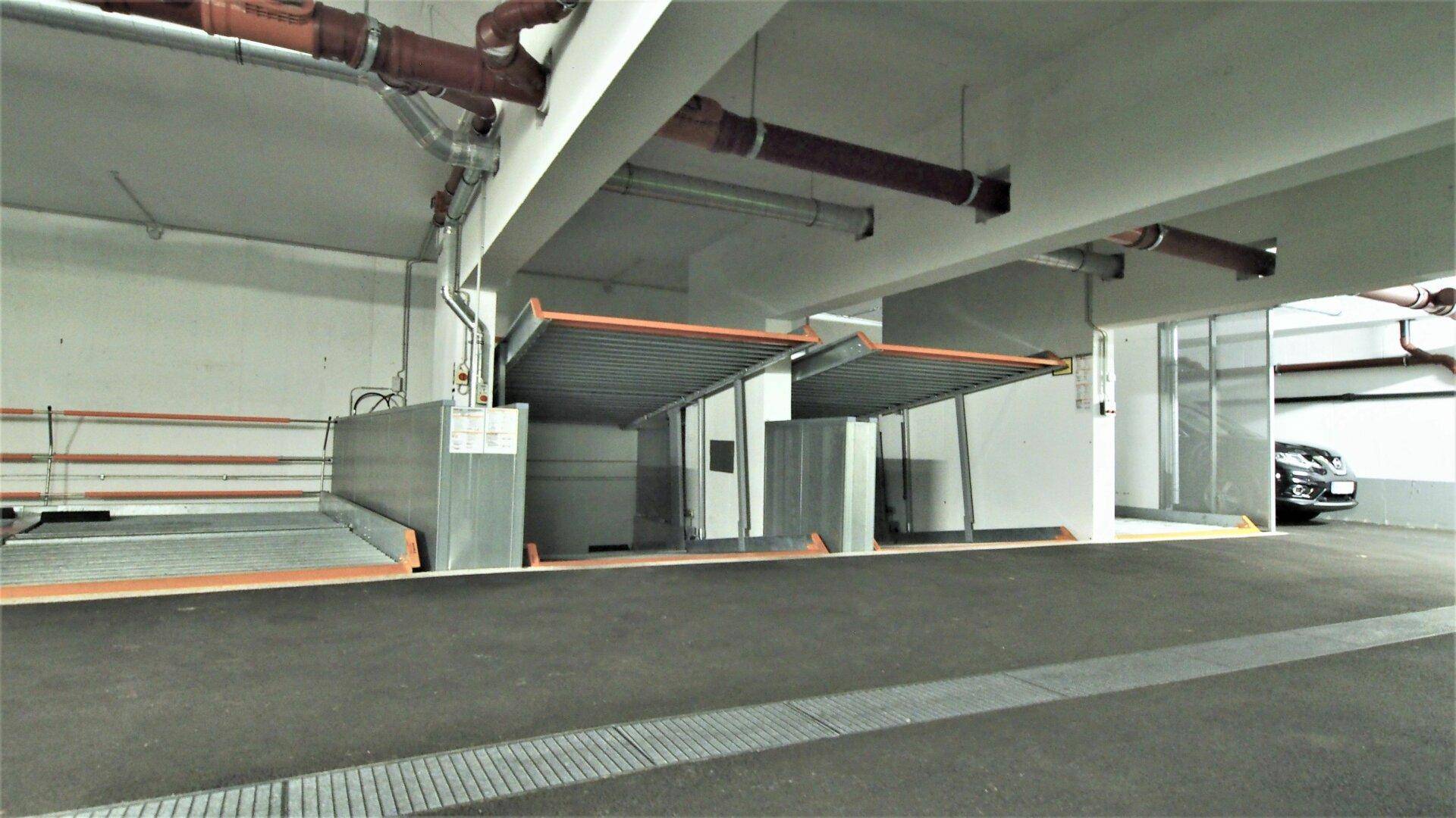 Tiefgarage mit mehreren mechanischen Parkplätzen und sichtbaren Rohrleitungen.