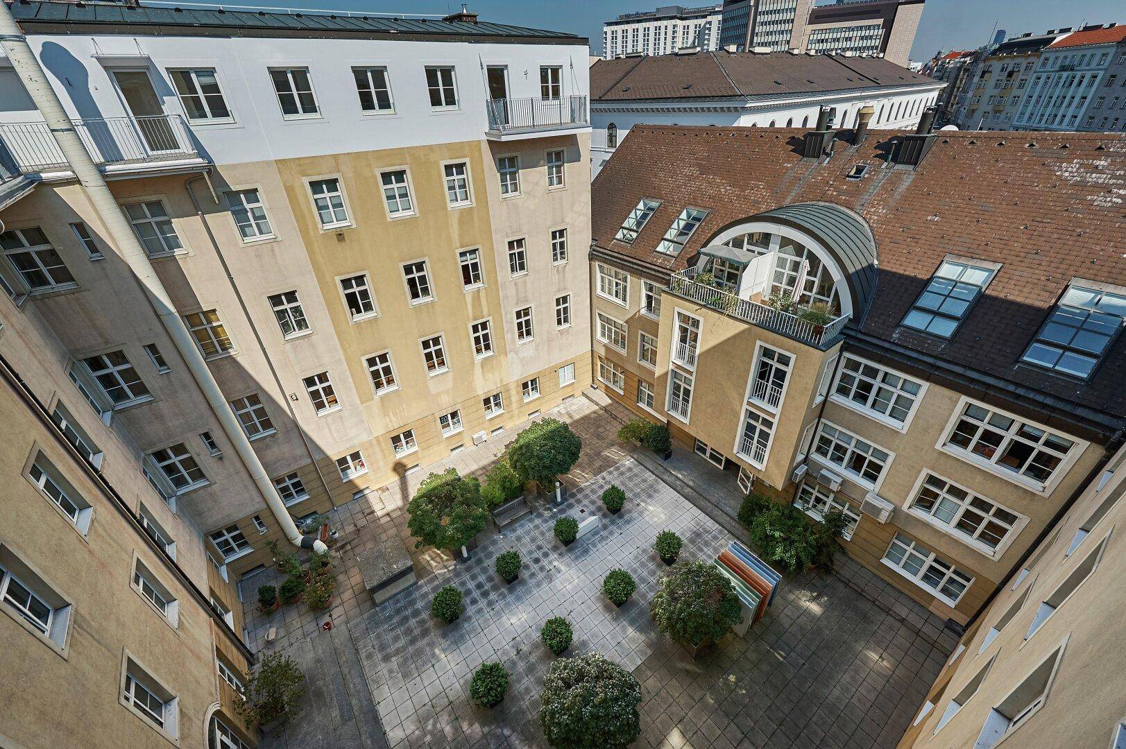 Blick von oben auf einen begrünten Innenhof, umgeben von Wohngebäuden mit Balkonen.