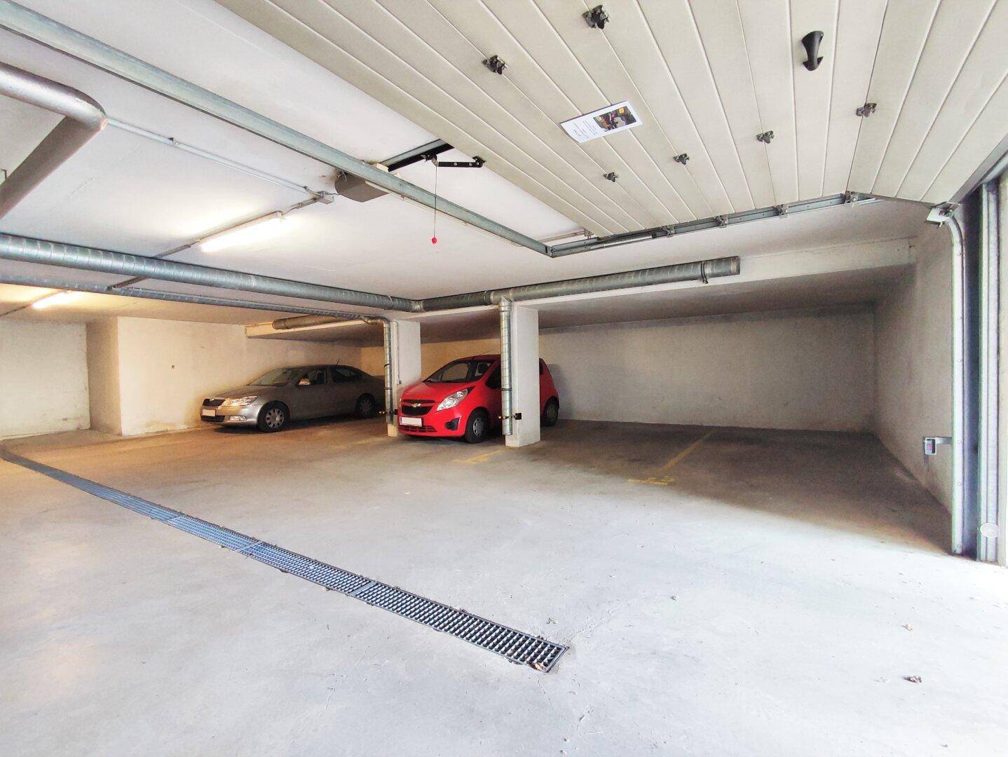 Helle Tiefgarage mit mehreren Stellplätzen und einem geöffneten Garagentor.