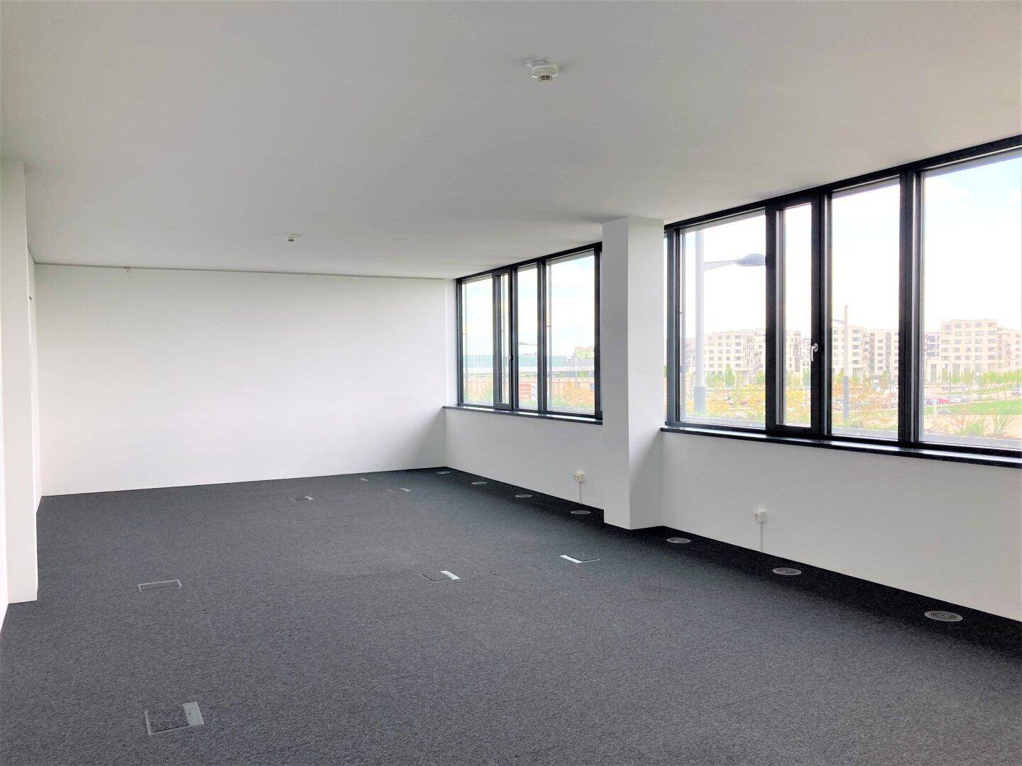Heller Bürobereich mit Teppichboden und großen Fenstern, die eine weite Aussicht auf die Umgebung bieten.