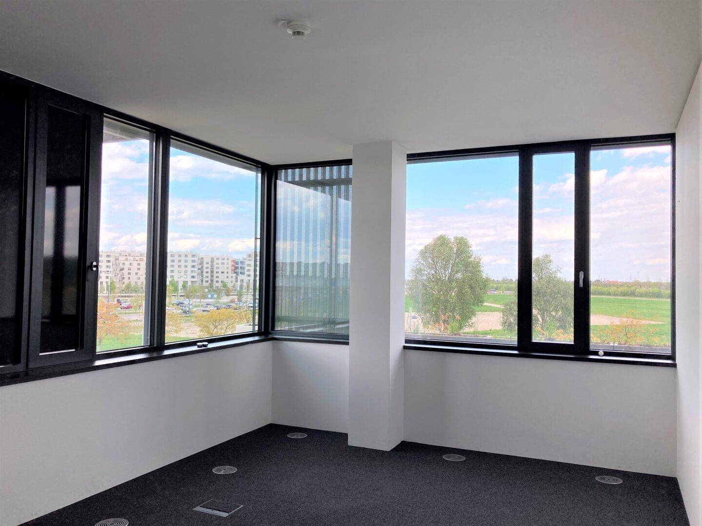 Eckbüro mit großen Fenstern, die einen weiten Blick auf die grüne Landschaft und die umliegenden Gebäude ermöglichen.