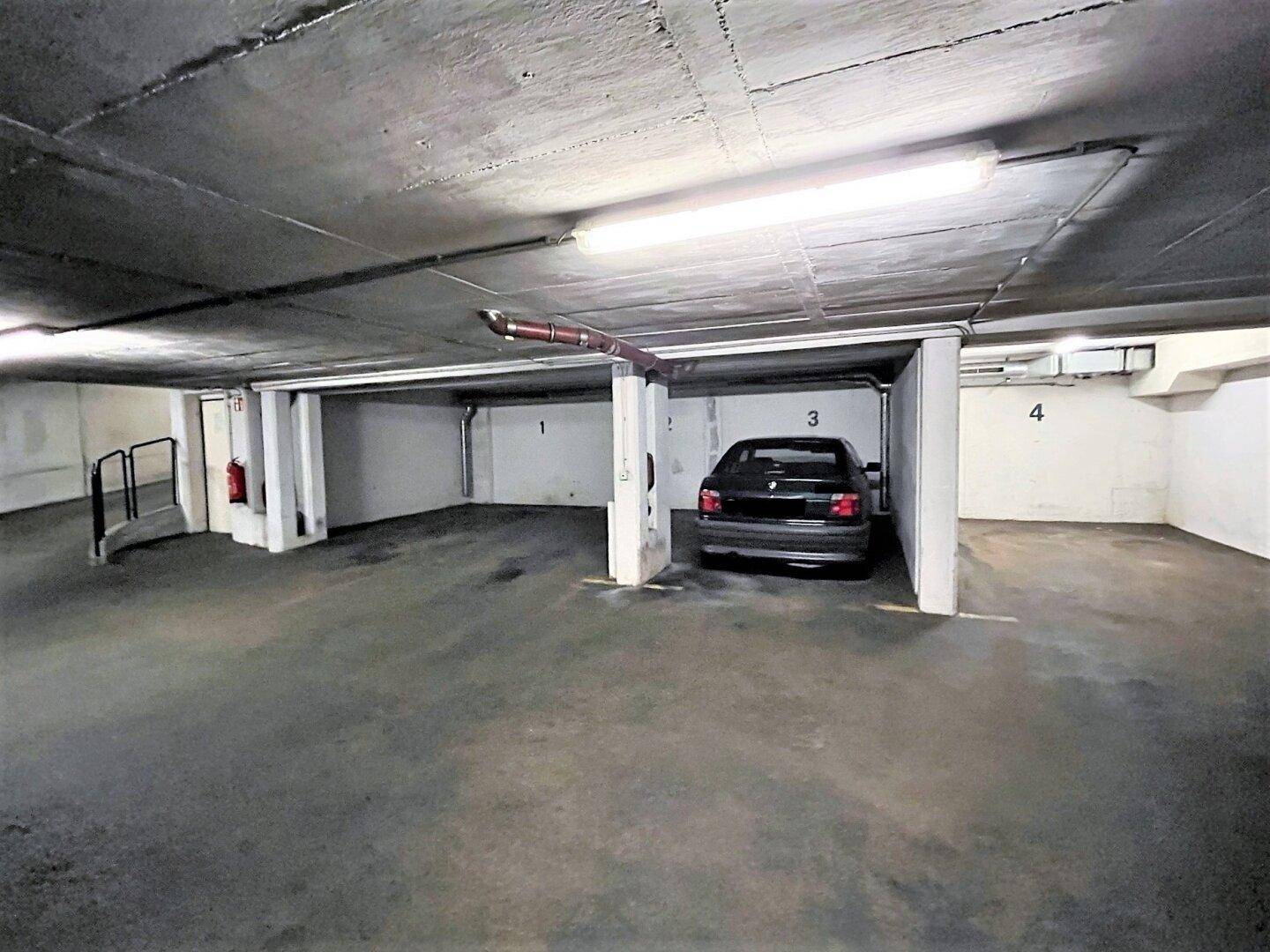 Eine Tiefgarage mit einem geparkten Auto, nummerierten Stellplätzen und Betonwänden.