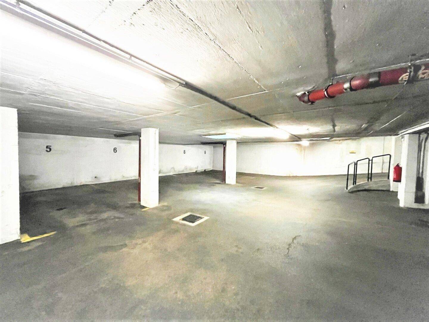 Eine leere Tiefgarage mit Betonboden, tragenden Säulen und Beleuchtung, bereit für die Nutzung.