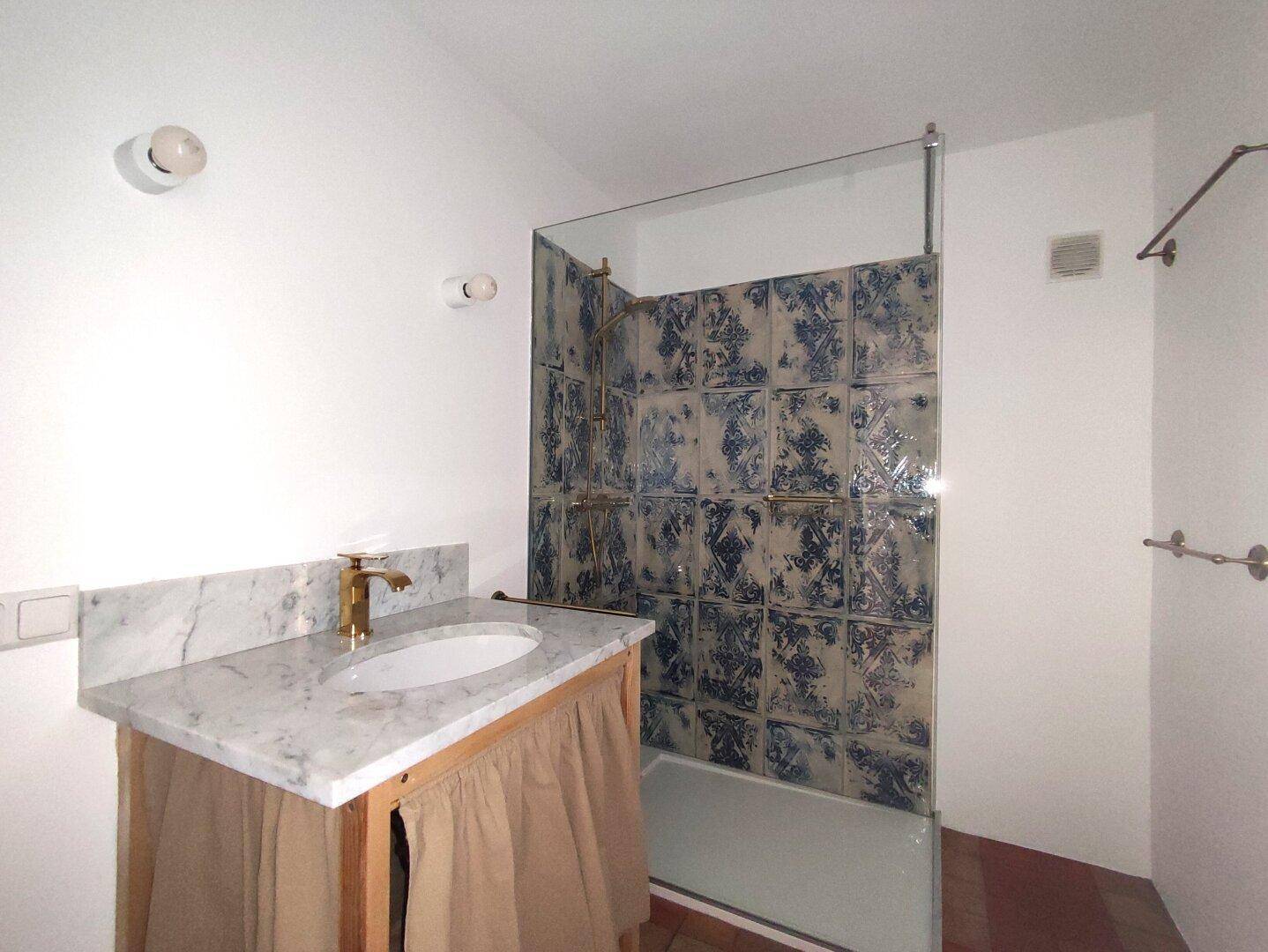 Badezimmer mit Marmorwaschtisch, goldener Armatur und Badewanne mit Duschwand.