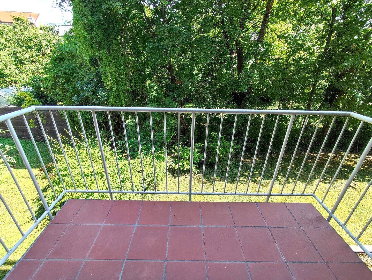 Balkon mit roten Fliesen und Blick auf den grünen Gartenbereich.