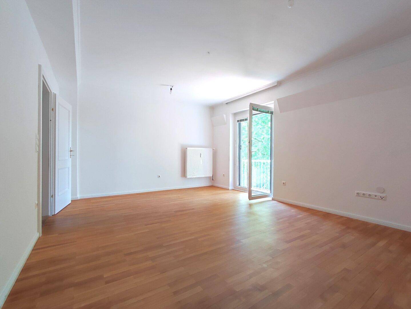Lichtdurchfluteter Wohnbereich mit Parkettboden, weißen Wänden und Balkonzugang.