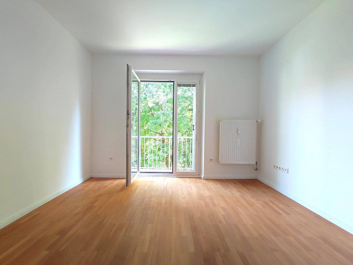 Heller, leerer Raum mit Parkettboden und Zugang zu einem kleinen Balkon.