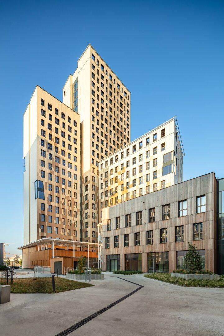 Zeitgenössische Architektur mit hohen Gebäuden und Holzverkleidung, eingebettet in eine städtische Umgebung mit klarem Himmel.