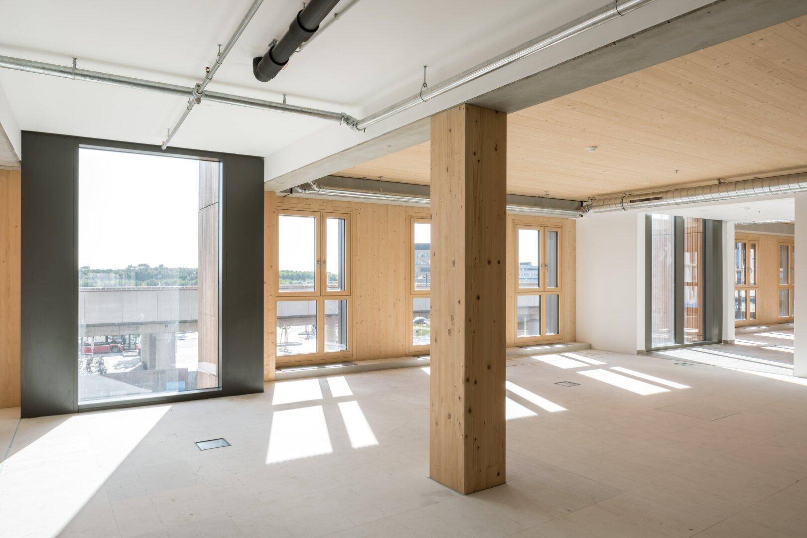 Heller Innenraum mit Holzbalken, großen Fenstern und sichtbaren Installationen, bereit für den Ausbau und die Gestaltung.