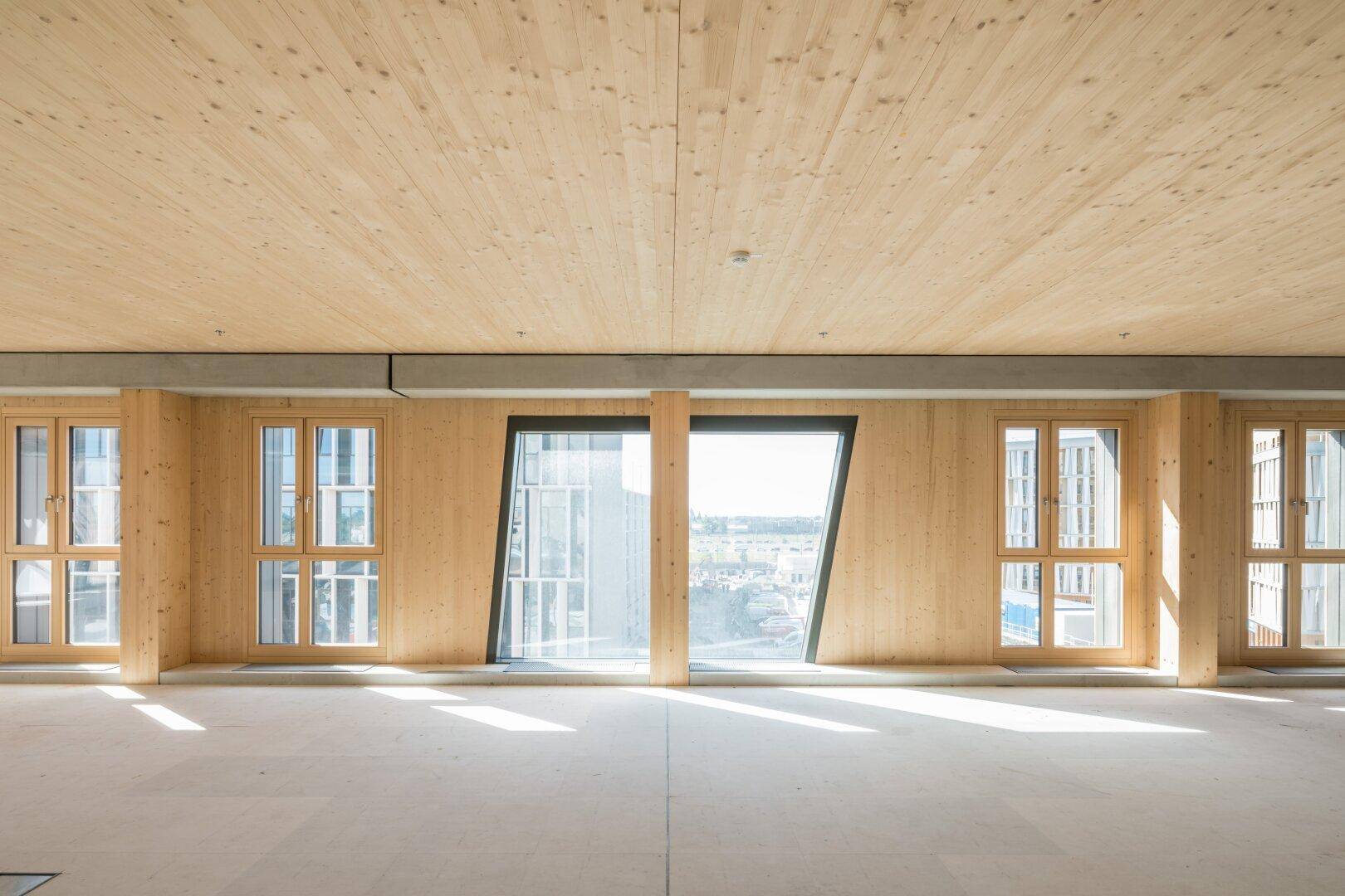Langer, heller Raum mit Holzbalkendecke und einer Reihe von Fenstern, die eine weite Aussicht bieten und viel Licht spenden.