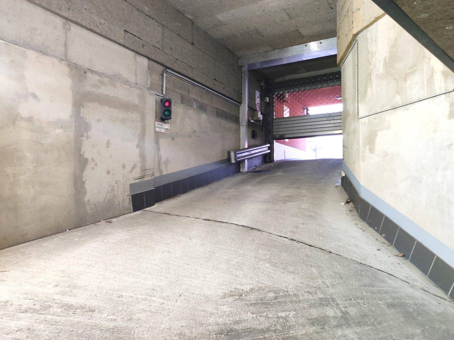 Betonrampe führt in eine Tiefgarage, mit Ampel zur Verkehrsregelung.