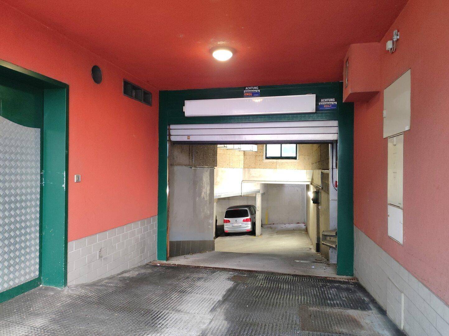 Einfahrt zur Tiefgarage mit roter Wandfarbe und einem Rolltor.