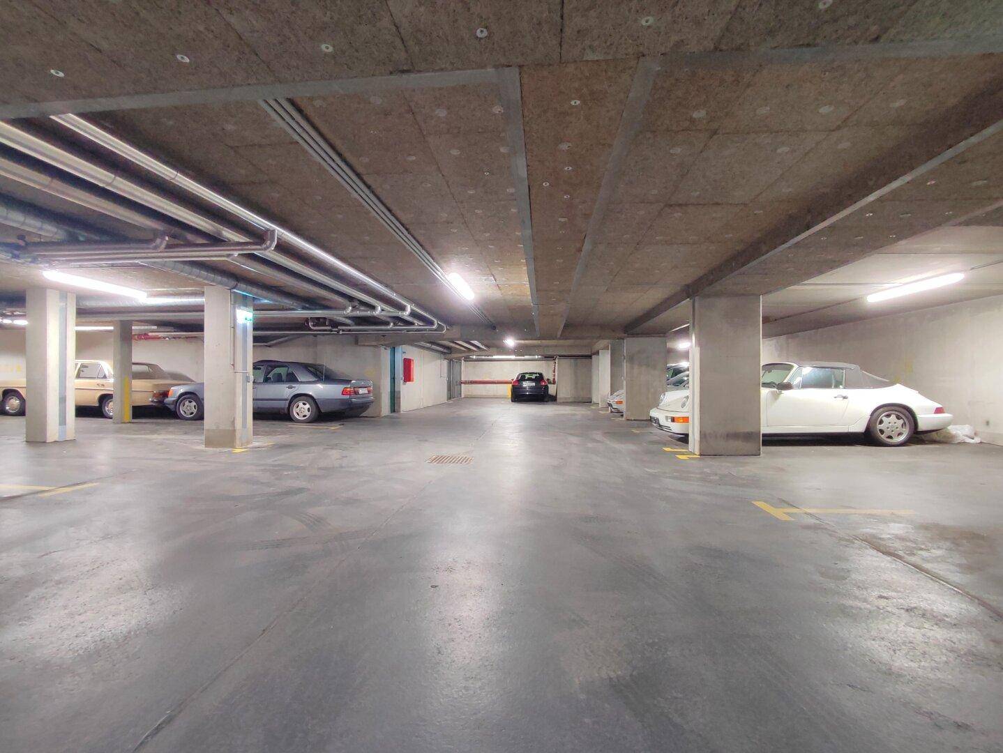 Geräumige Tiefgarage mit mehreren geparkten Fahrzeugen und Betonwänden.