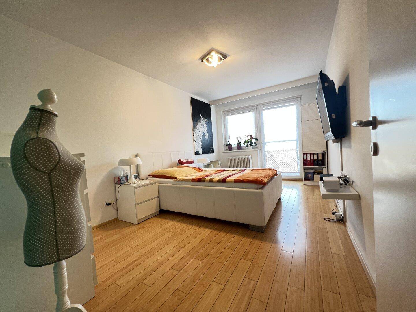 Helles Schlafzimmer mit Holzboden, Doppelbett und Wandfernseher.