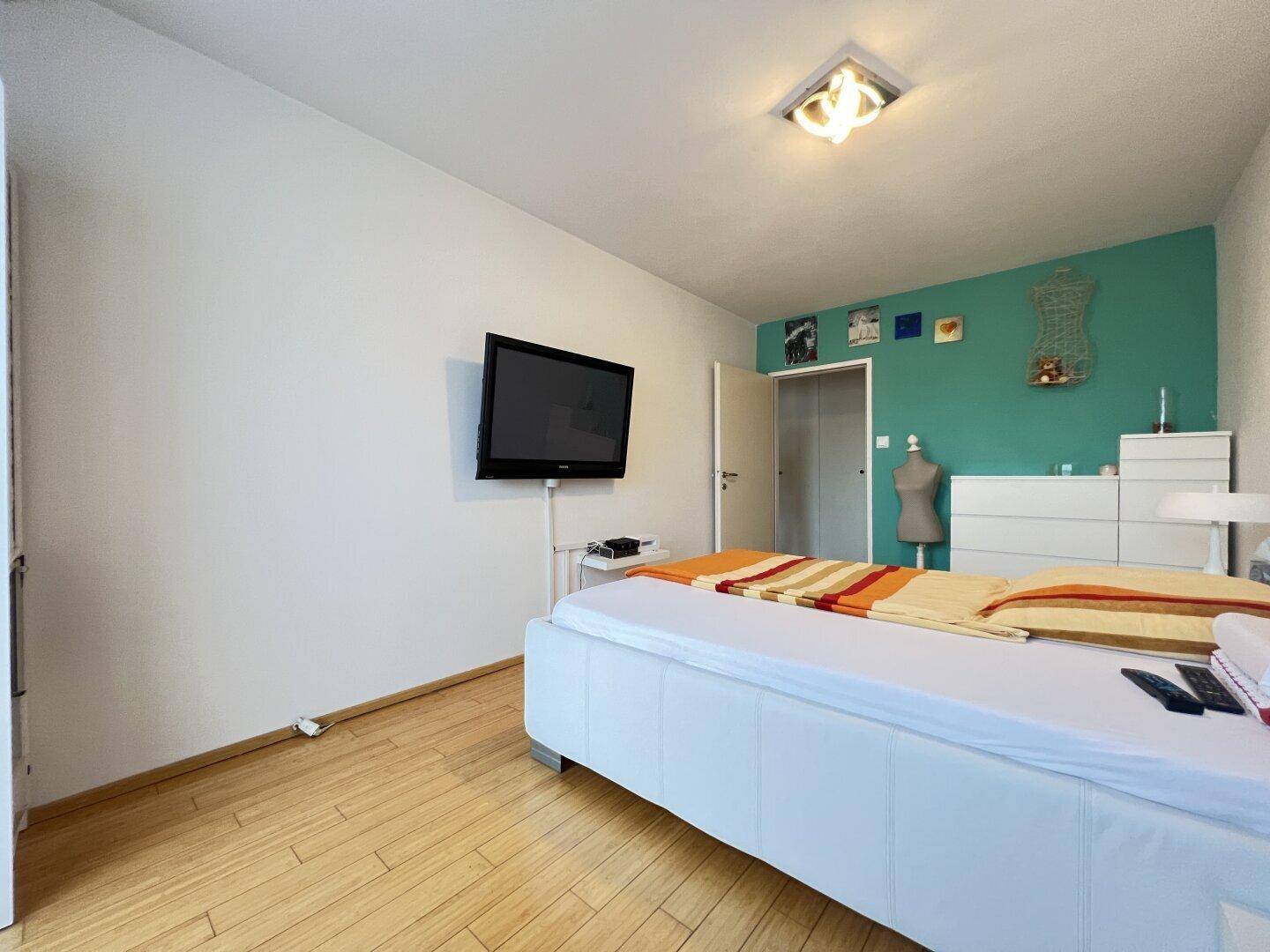Schlafzimmer mit Holzboden, weißem Bett und einer farbigen Akzentwand.