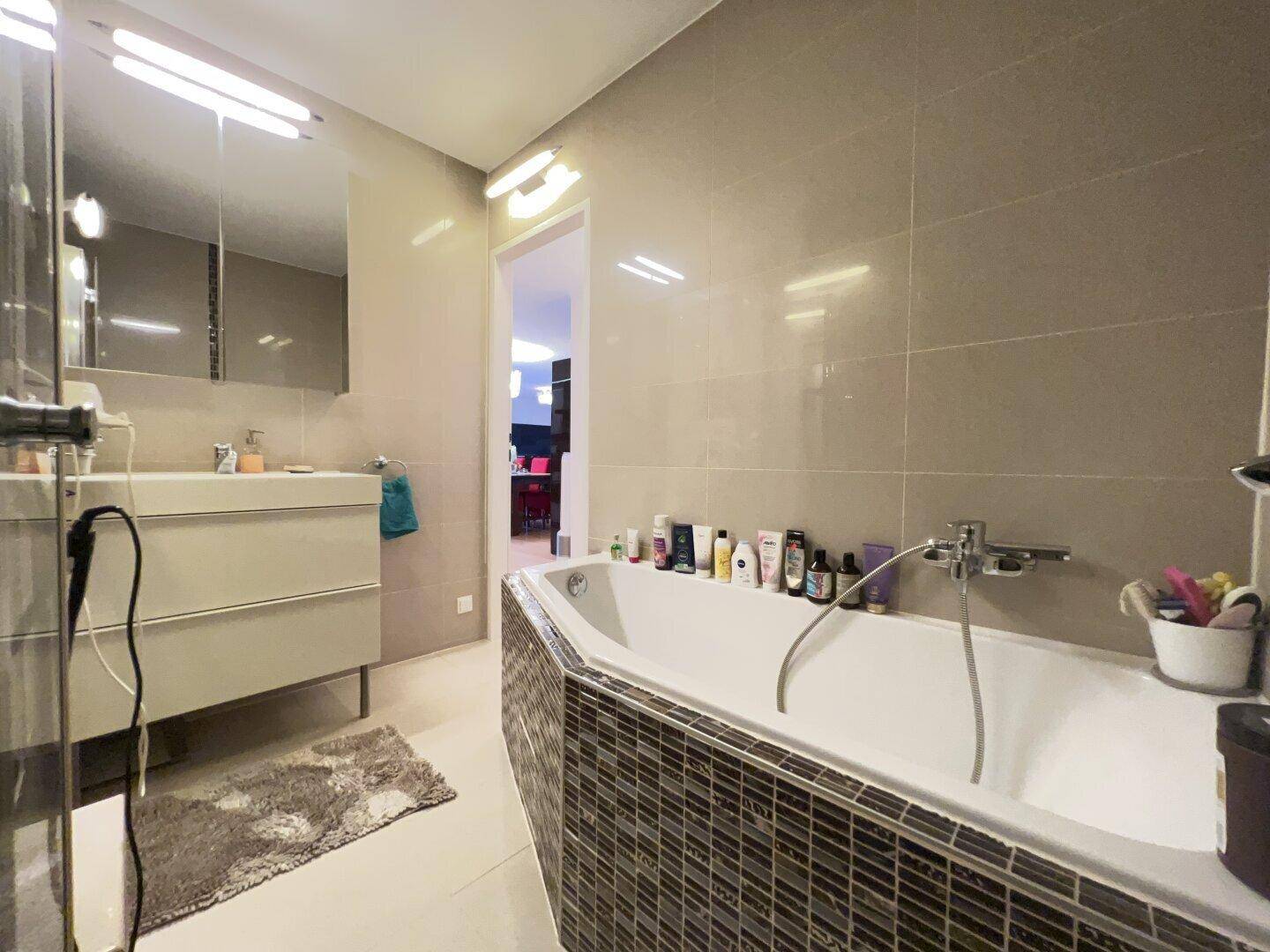 Badezimmer mit Badewanne, Waschtisch und großen beigefarbenen Wandfliesen.