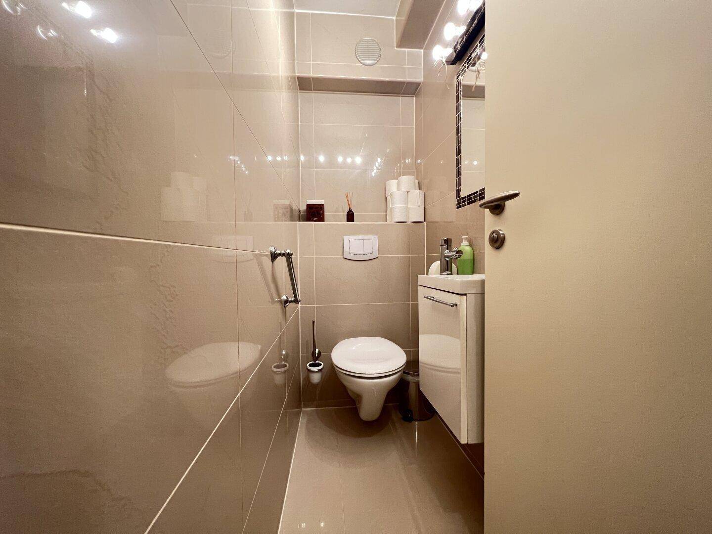 Kleines Gäste-WC mit Wand-WC, Waschbecken und beigefarbenen Fliesen.