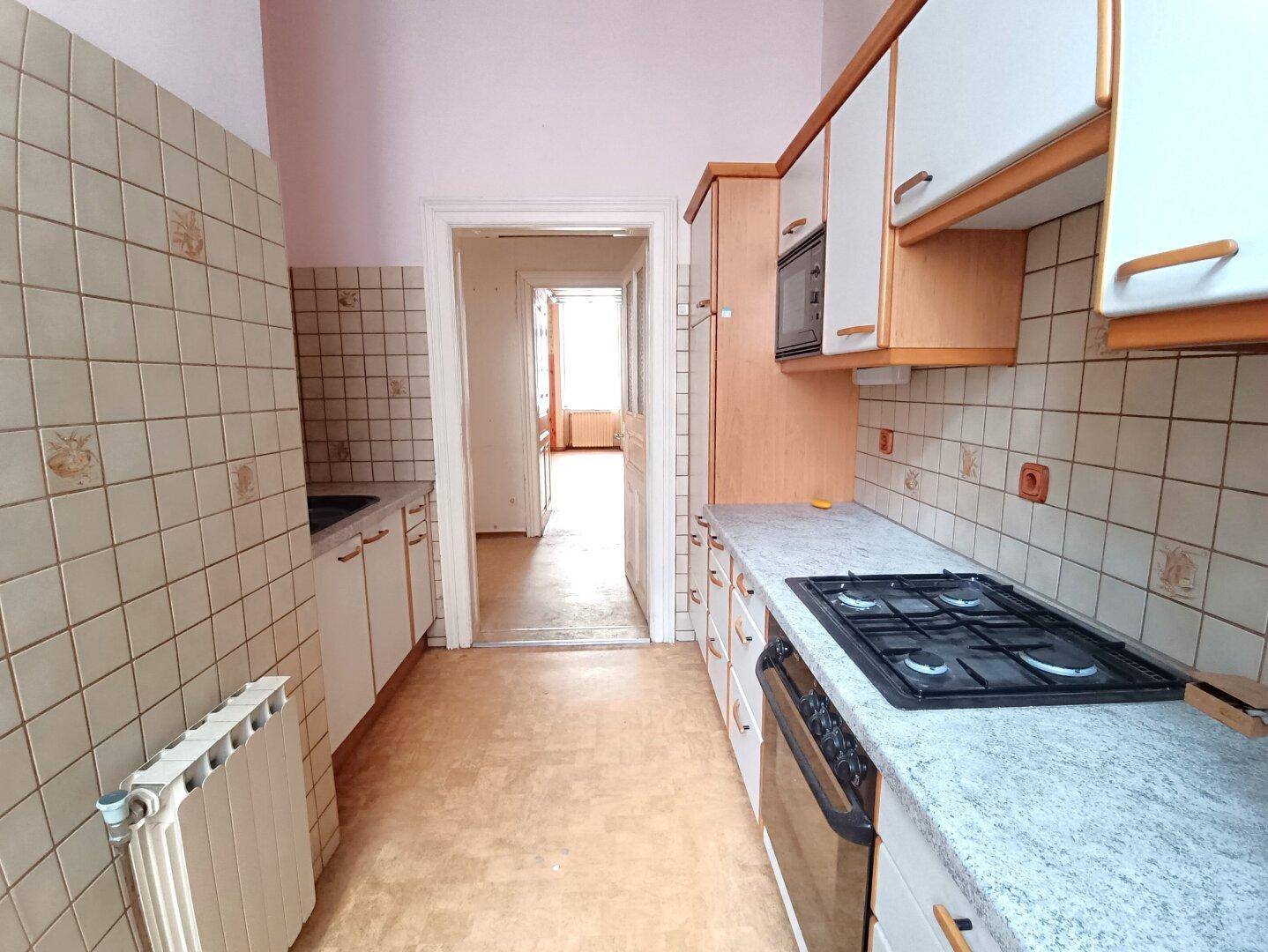 Ältere Küche mit Gasherd, gefliesten Wänden und Blick in einen weiteren Raum.