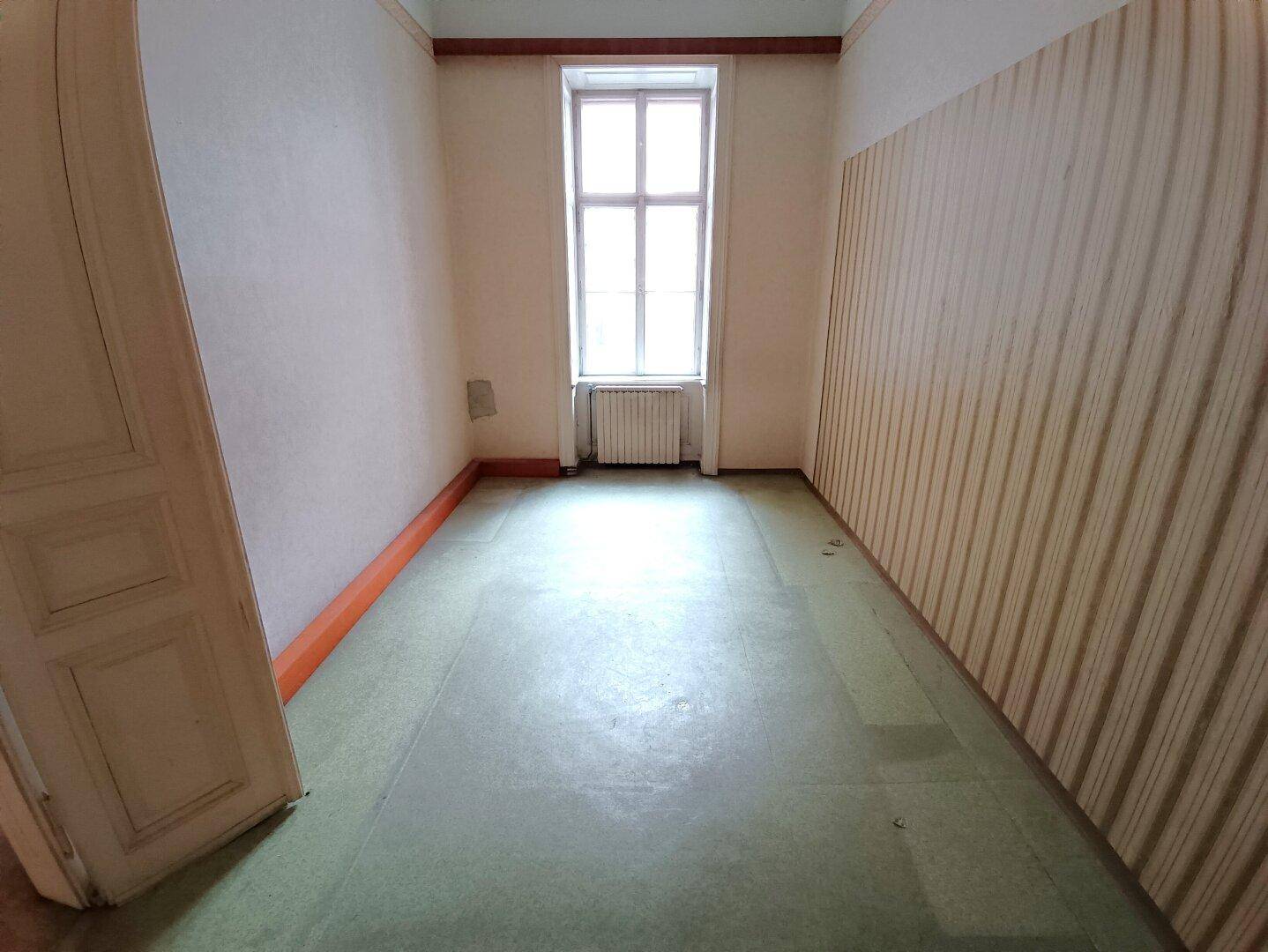 Leerer Raum mit Fenster, grünem Bodenbelag und gestreifter Tapete an einer Wand.