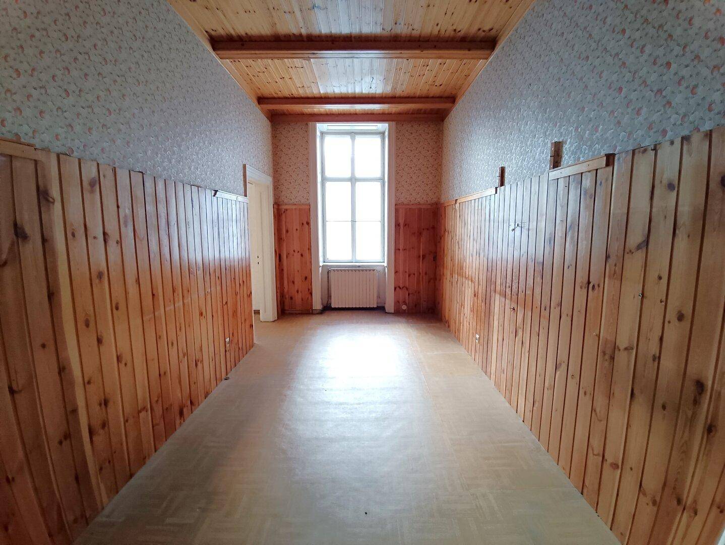 Raum mit Holzvertäfelung an Wänden und Decke, einem Fenster und hellem Bodenbelag.