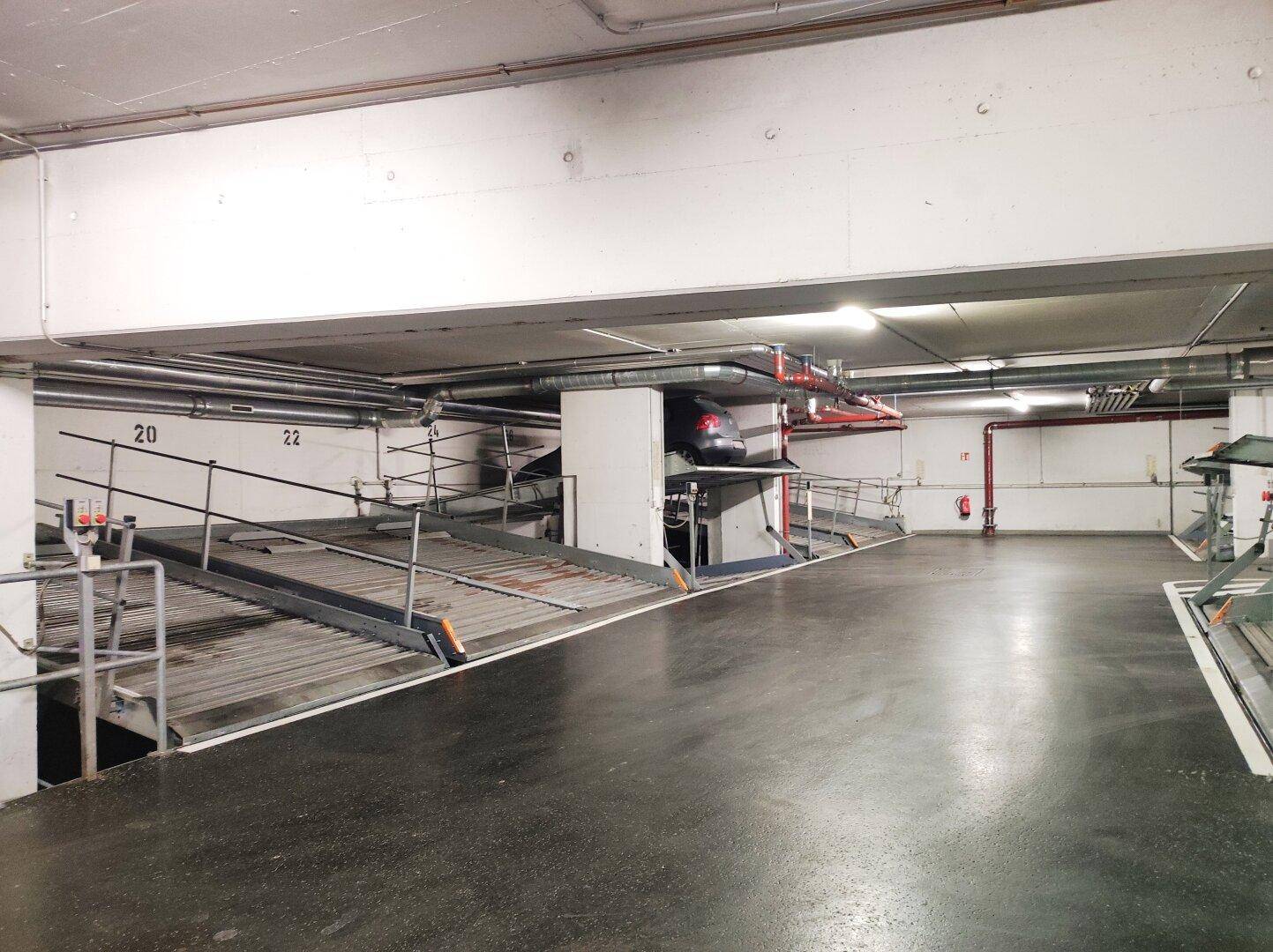 Tiefgarage mit modernen Doppelparkern und sichtbaren Installationen an der Decke und Wänden.