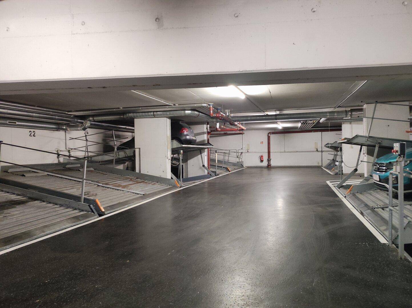 Blick in eine Tiefgarage mit mehreren Doppelparkern und einem geparkten Fahrzeug auf einer Plattform.