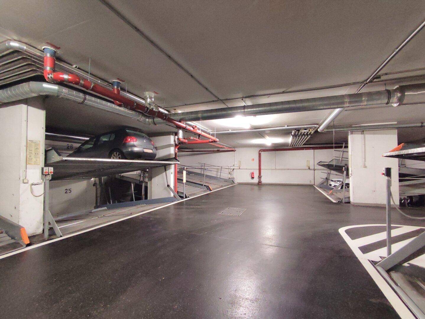 Weitwinkelaufnahme einer Tiefgarage mit mehreren Doppelparkern und einem geparkten Fahrzeug auf der oberen Ebene.