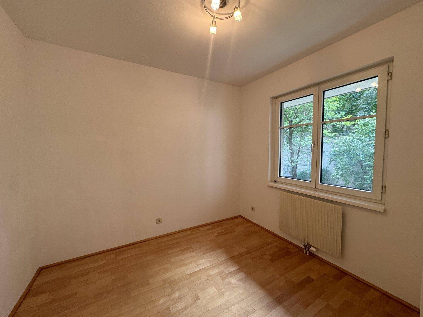 Kleines, helles Schlafzimmer mit Parkettboden und einem Fenster, das viel natürliches Licht spendet.
