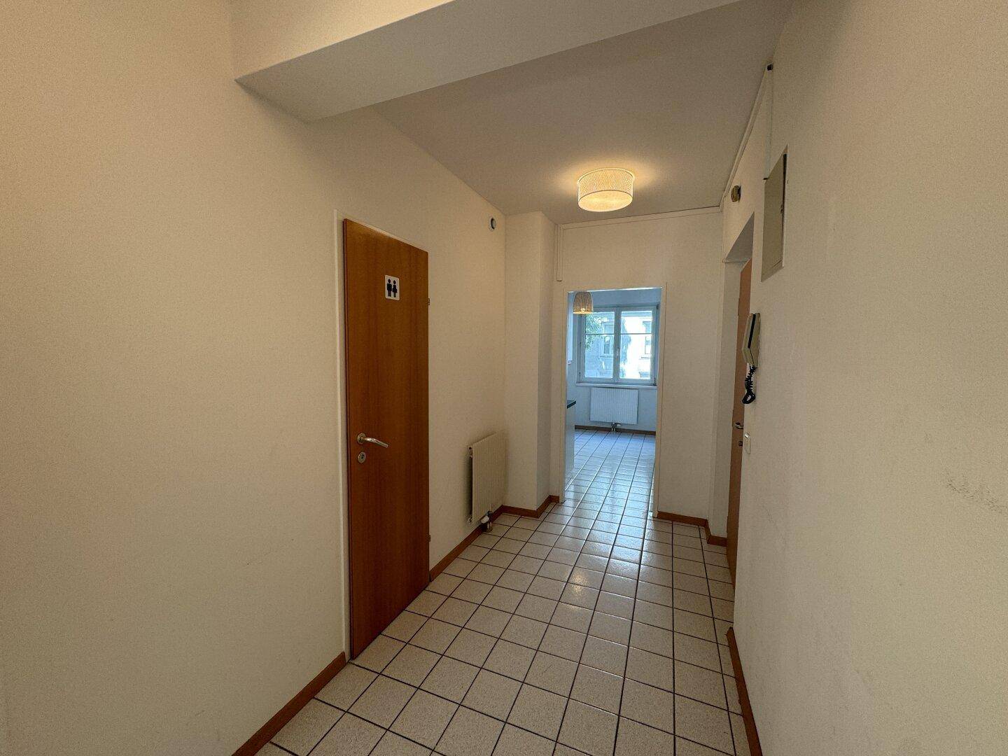 Heller Flur mit Fliesenboden und einer Tür, die zu einem Badezimmer oder einer Toilette führt.