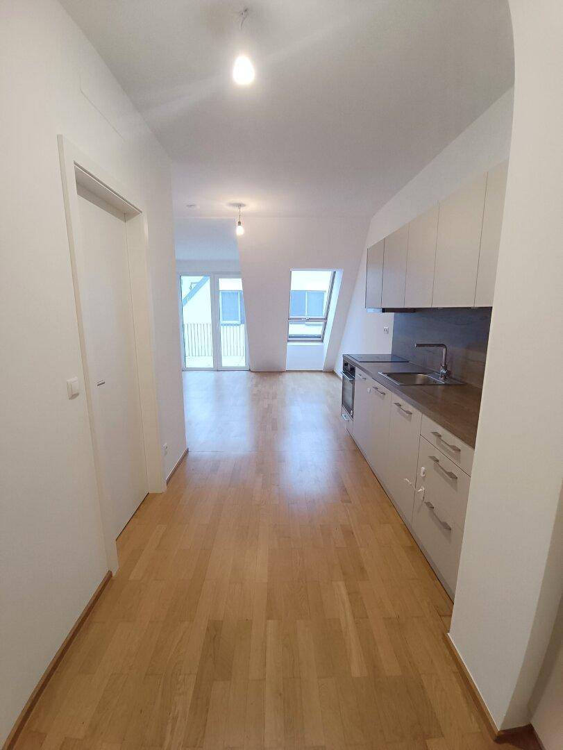 Geräumiger Wohnbereich mit offener Küchenzeile, Parkettboden und Zugang zum Balkon.