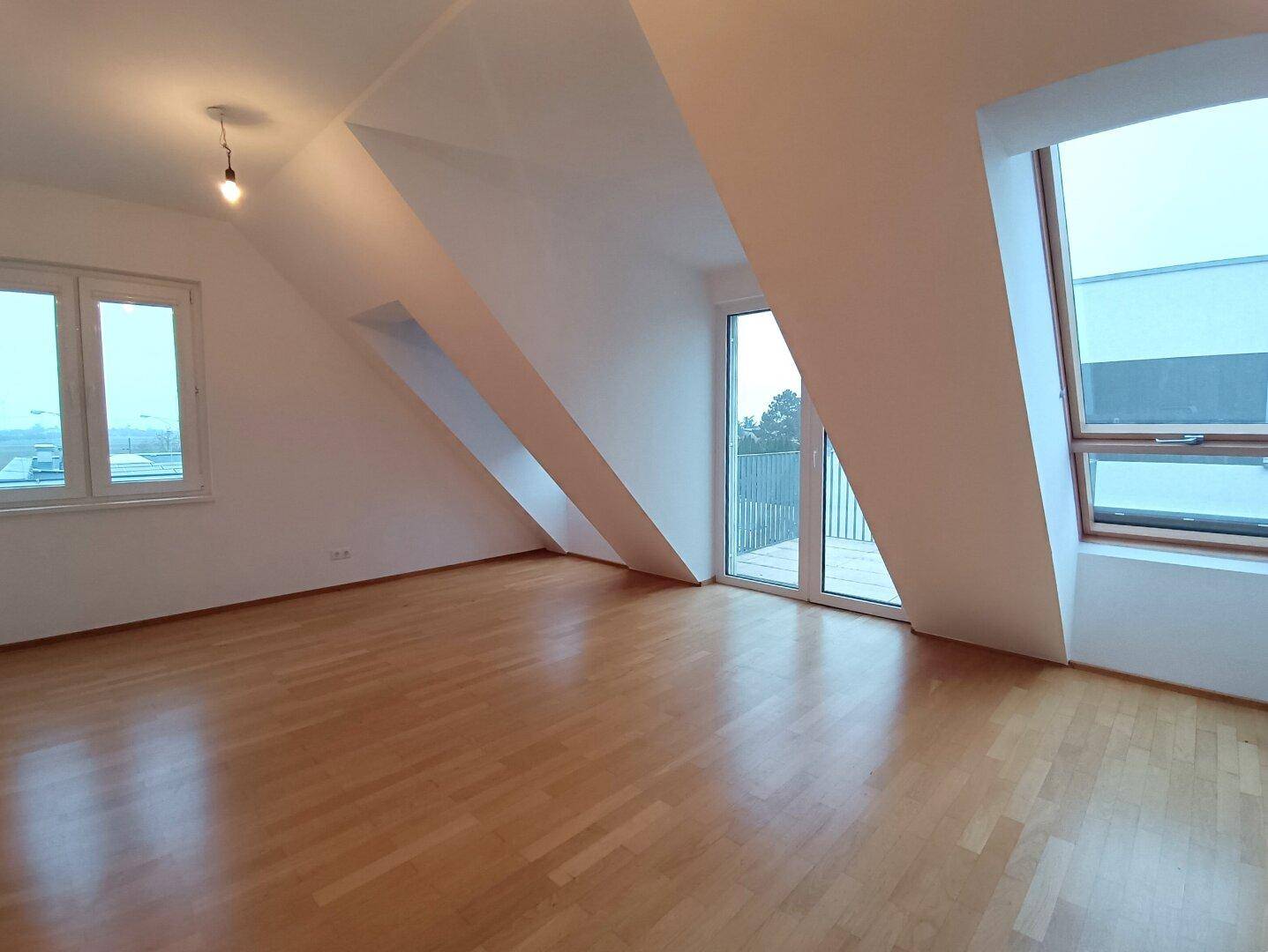 Heller Wohnbereich mit Dachschrägen, Parkettboden und Zugang zu einem Balkon.