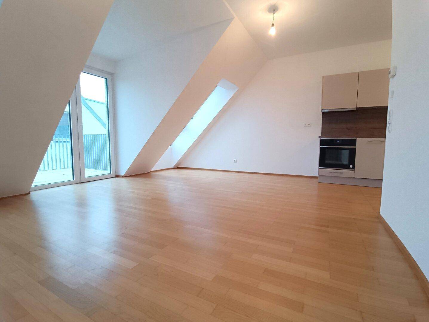 Offener Wohnbereich mit integrierter Küchenzeile, Parkettboden und viel Tageslicht durch große Fenster.
