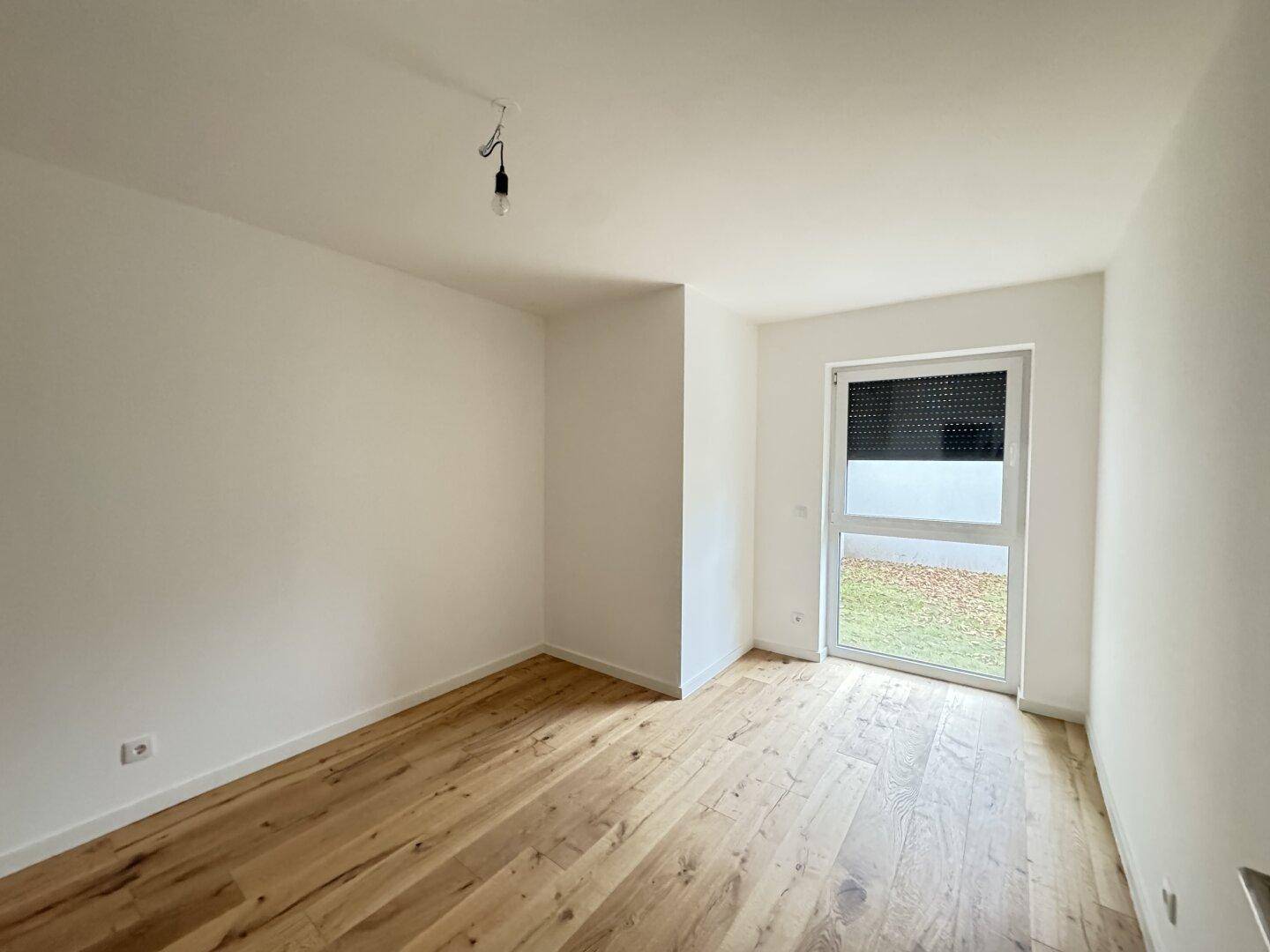 Helles Zimmer mit neuem Holzboden und Zugang zum Gartenbereich durch eine große Tür.