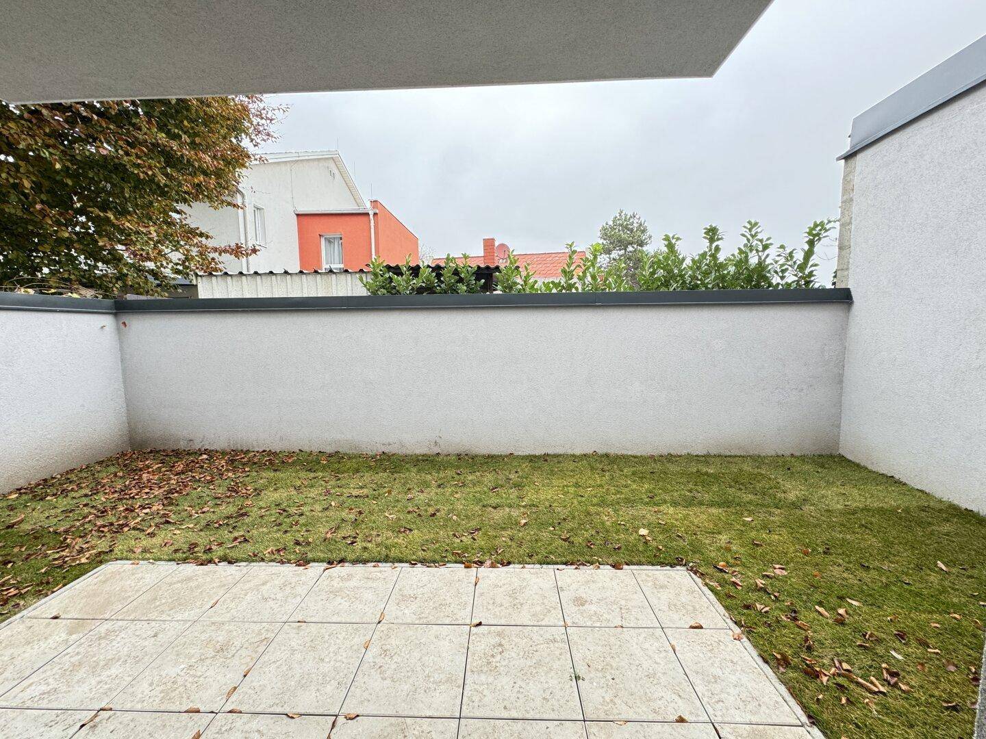 Kleiner, ummauerter Gartenbereich mit Rasenfläche und einer gepflasterten Terrasse.
