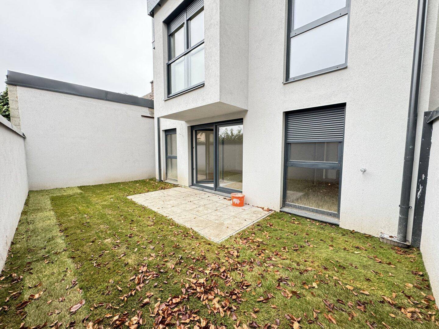 Blick auf den kleinen Garten mit Terrasse und Zugang zum Gebäude durch große Glastüren.