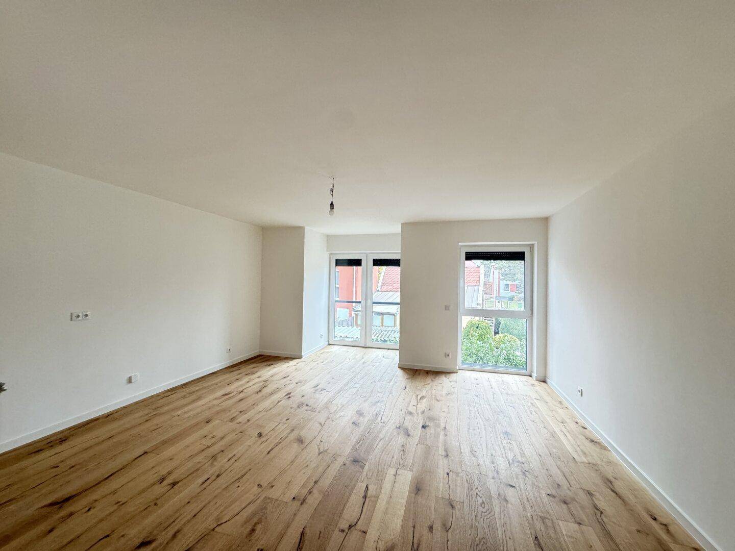 Helles, leeres Wohnzimmer mit neuem Holzboden und großen Fenstern, bereit zum Einzug.