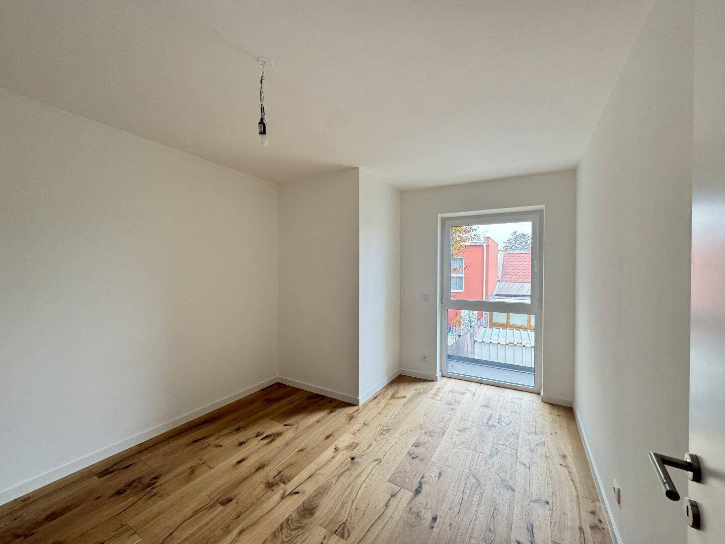 Leeres Schlafzimmer mit Holzboden und Fenster, das viel Tageslicht hereinlässt.