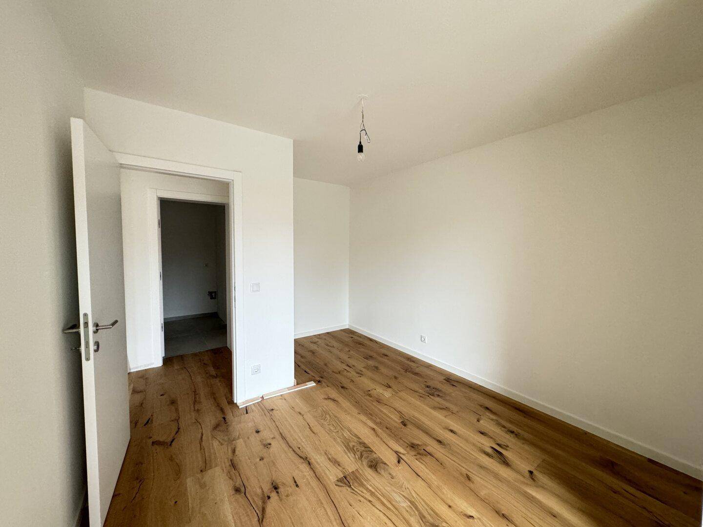Unmöbliertes Zimmer mit Holzboden und weiß gestrichenen Wänden, ideal als Schlaf- oder Arbeitszimmer.