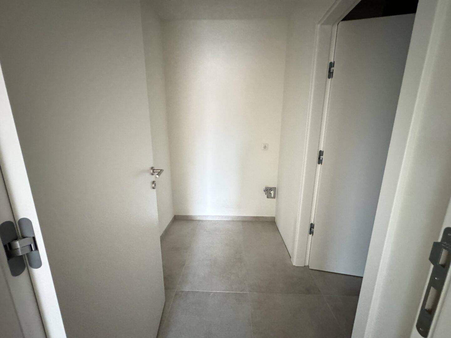 Kleiner Hauswirtschaftsraum mit Fliesenboden und Anschlüssen, ideal für Waschmaschine und Trockner.