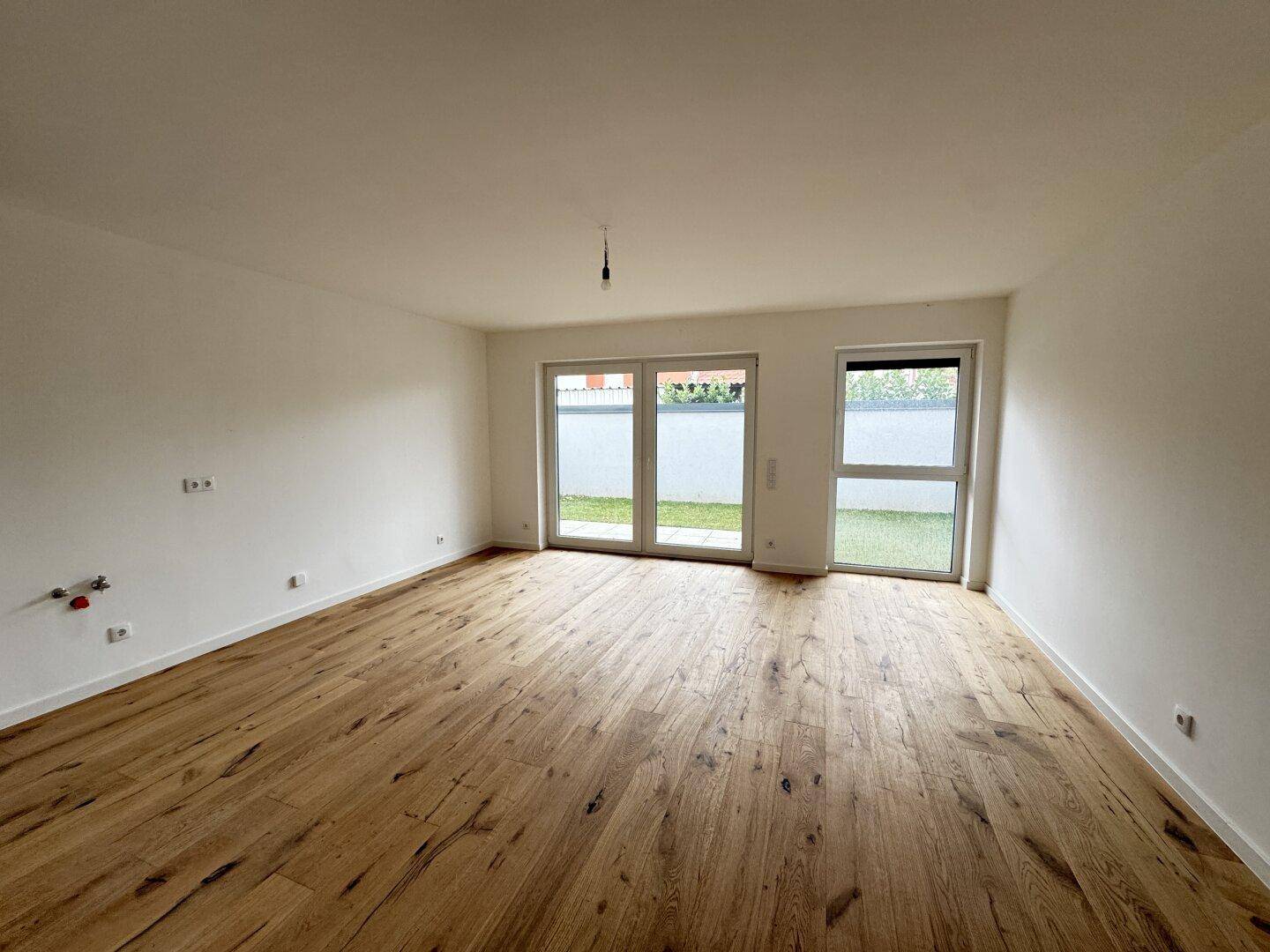 Heller, leerer Raum mit hochwertigem Holzboden und großen Fenstern, die direkten Zugang zum grünen Garten bieten.