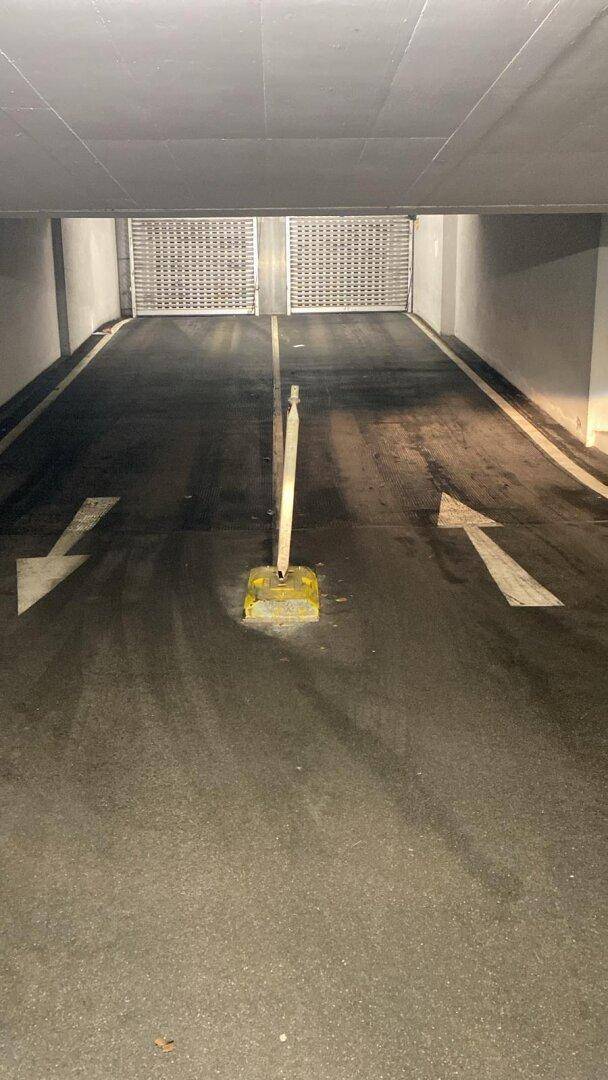 Zufahrtsrampe zu einer Tiefgarage mit Pfeilmarkierungen auf dem Boden und einem Rolltor am Ende.