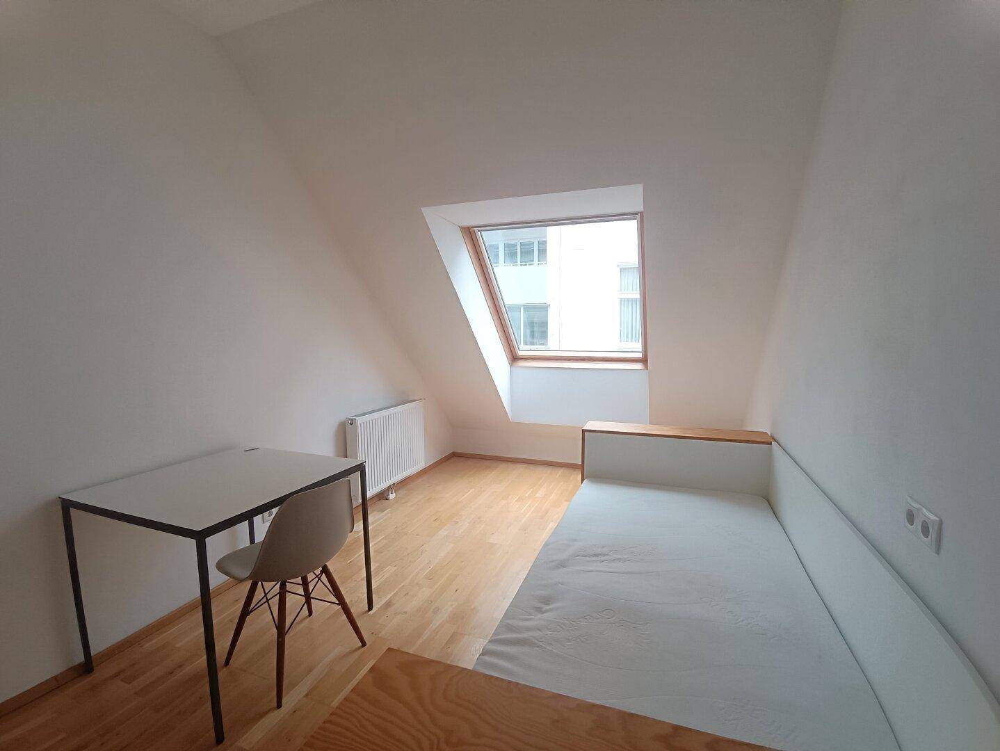 Helles Schlafzimmer im Dachgeschoss mit Dachfenster und Holzboden.