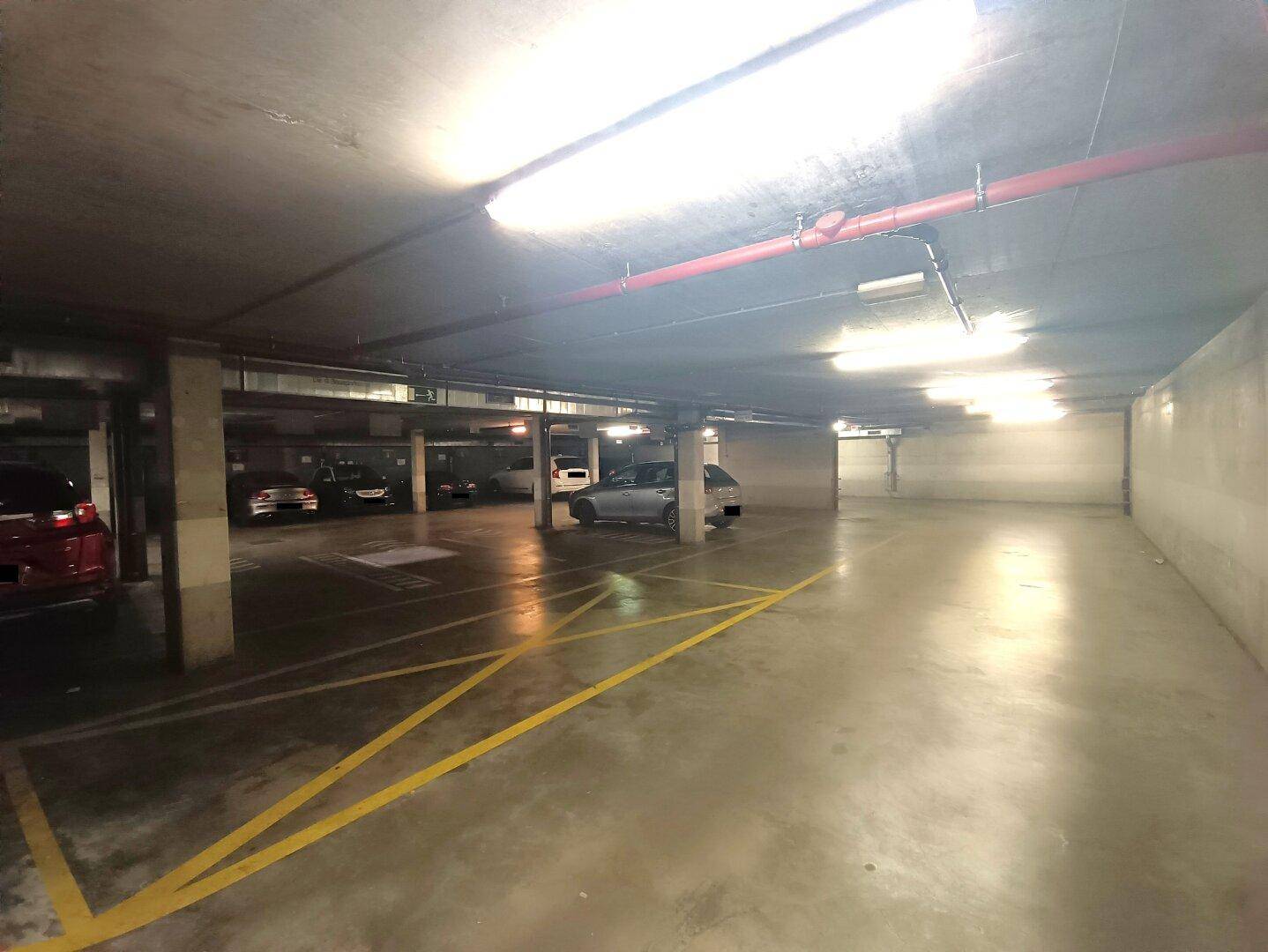 Geräumige Tiefgarage mit markierten Stellplätzen und einer Reihe von geparkten Autos im Hintergrund.