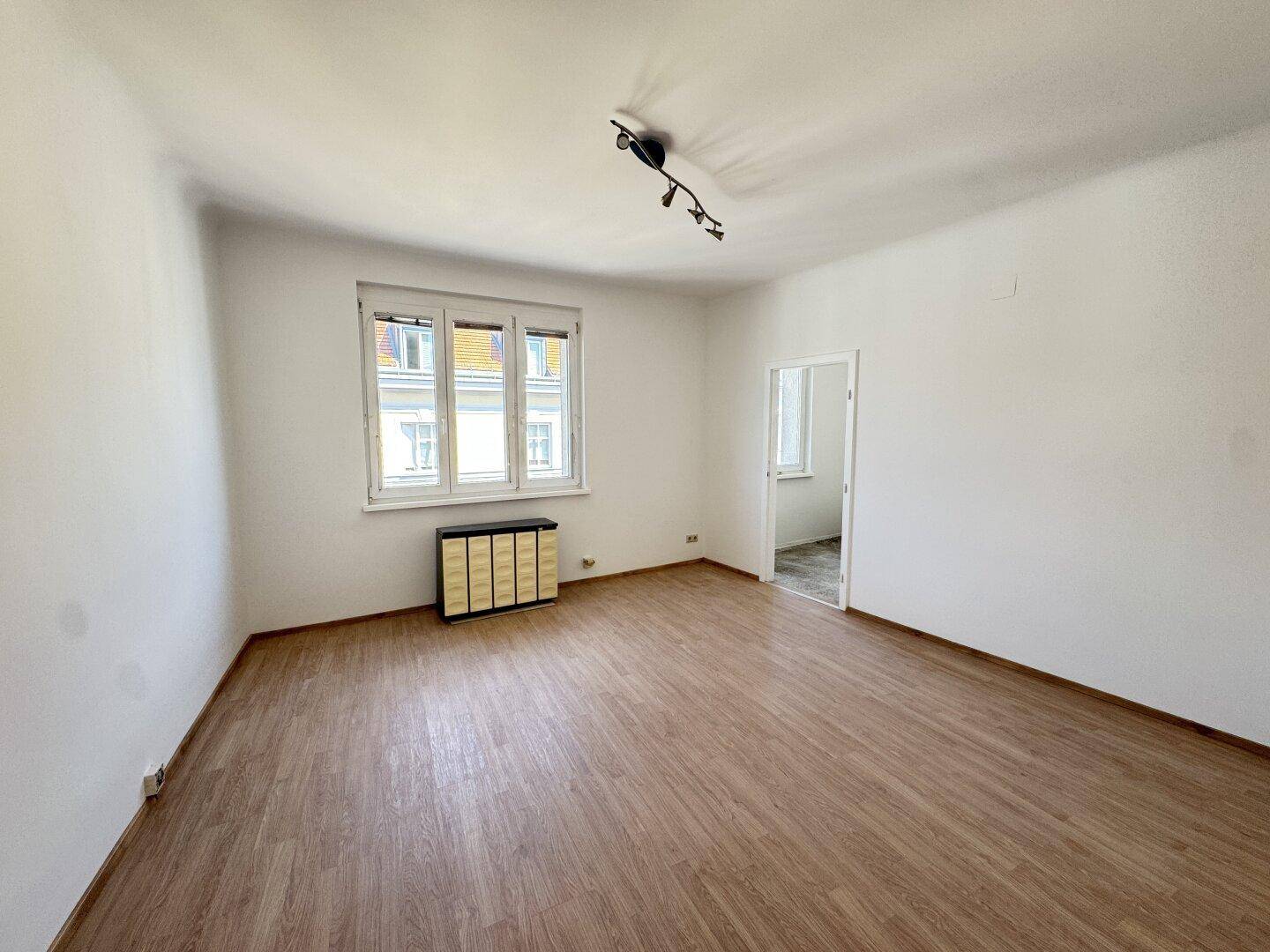 Heller, leerer Raum mit Laminatboden und weiß gestrichenen Wänden, bereit zur individuellen Gestaltung.