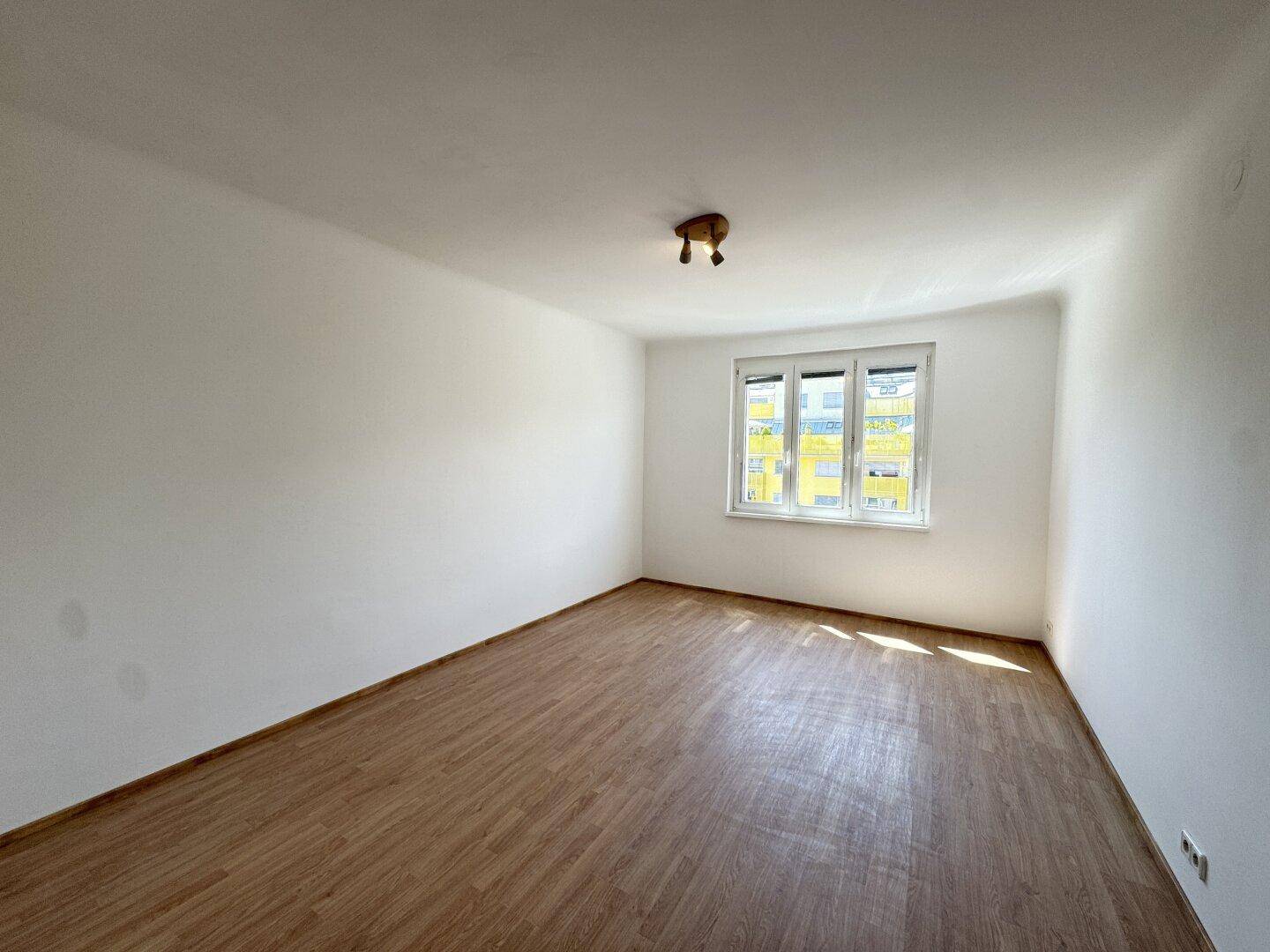 Geräumiges, helles Zimmer mit Laminatboden und Blick auf die Umgebung.